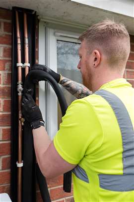 A plumber installs lagging to copper pipes on a residential property as part of a heatpump retrofit